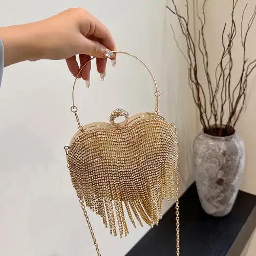 Gold beaded handbag with fringe held by a hand against a neutral background