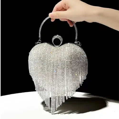 Heart-shaped handbag with crystal embellishments held by a hand against a black background