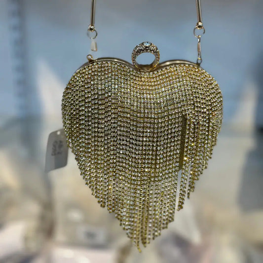 Heart-shaped handbag with rhinestone details held by a hand against a blurred background