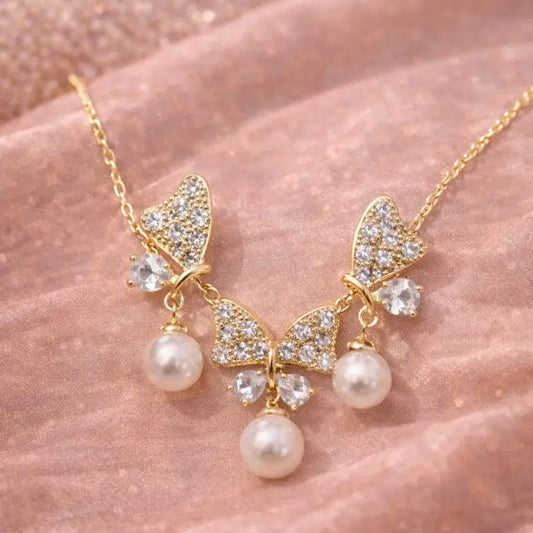 Gold necklace with butterfly design and pearls on a pink fabric background